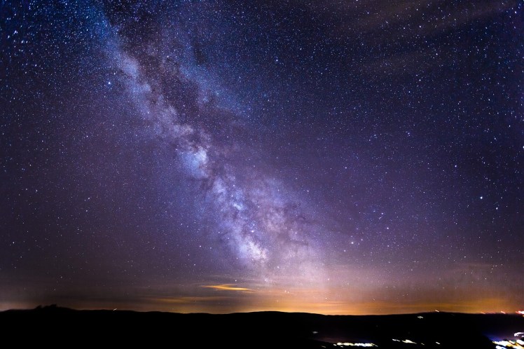 Imagen de un cielo estrellado sobre un horizonte. Gran parte de lo que se ve en el cielo es la Vía Láctea.